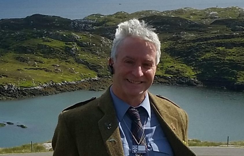 Man wearing a kilt and standing in front of a loch