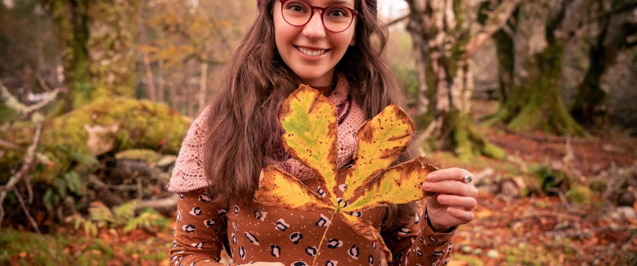 Woman standing among trees. holding a chestnut leaf in her hands