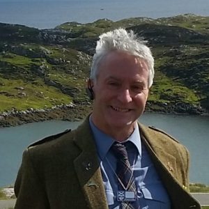 Man wearing a kilt and standing in front of a loch